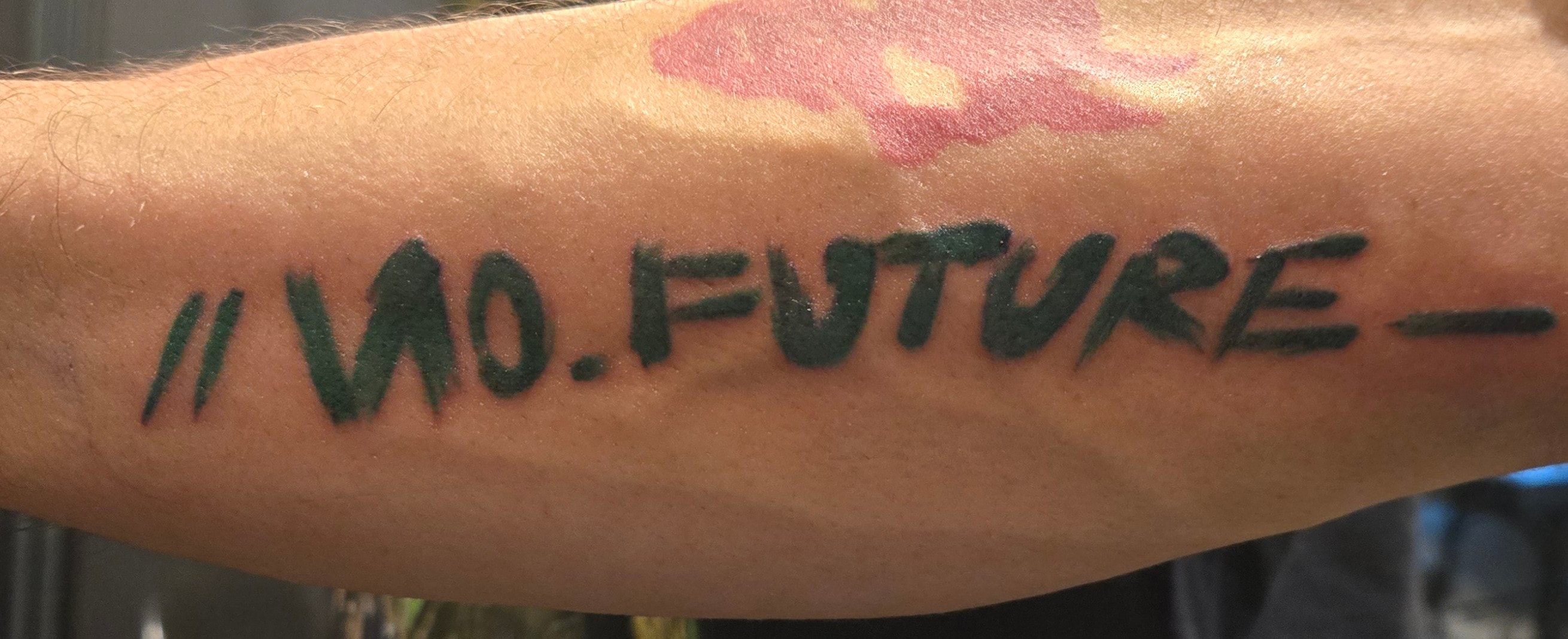 Bold black custom lettering tattoo reading No Future with a small red accent